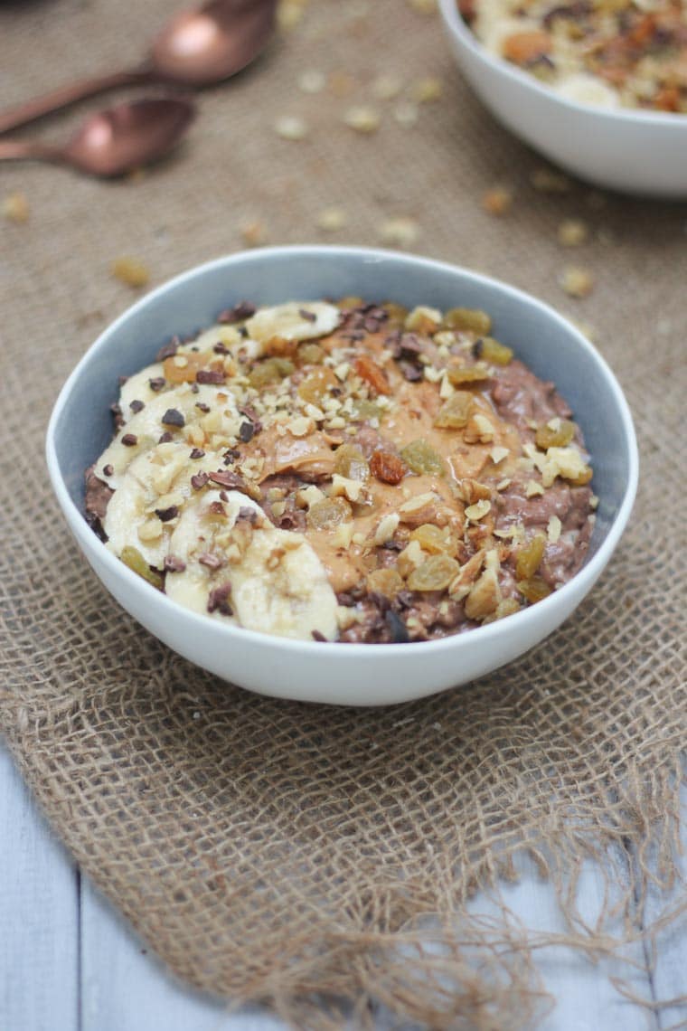 vegan chocolate zucchini oats in a blue and white bowl topped with fruit 