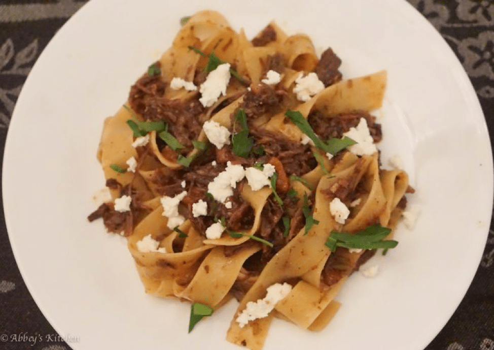 close up of short rib pasta garnished with herbs and cheese on a white plate