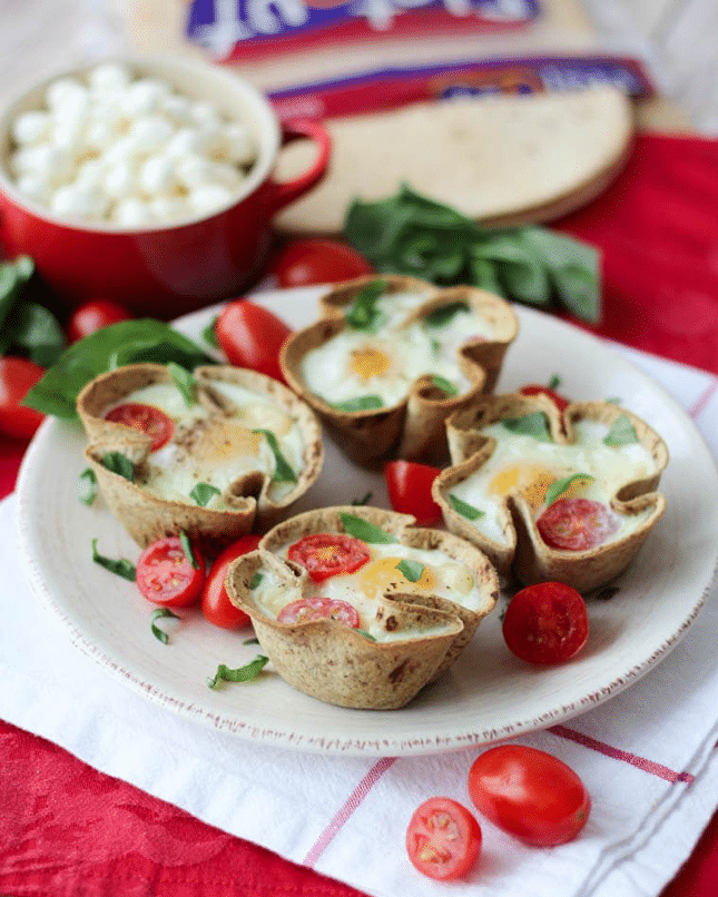 four caprese egg cups garnished with tomatoes and herbs on a white plate