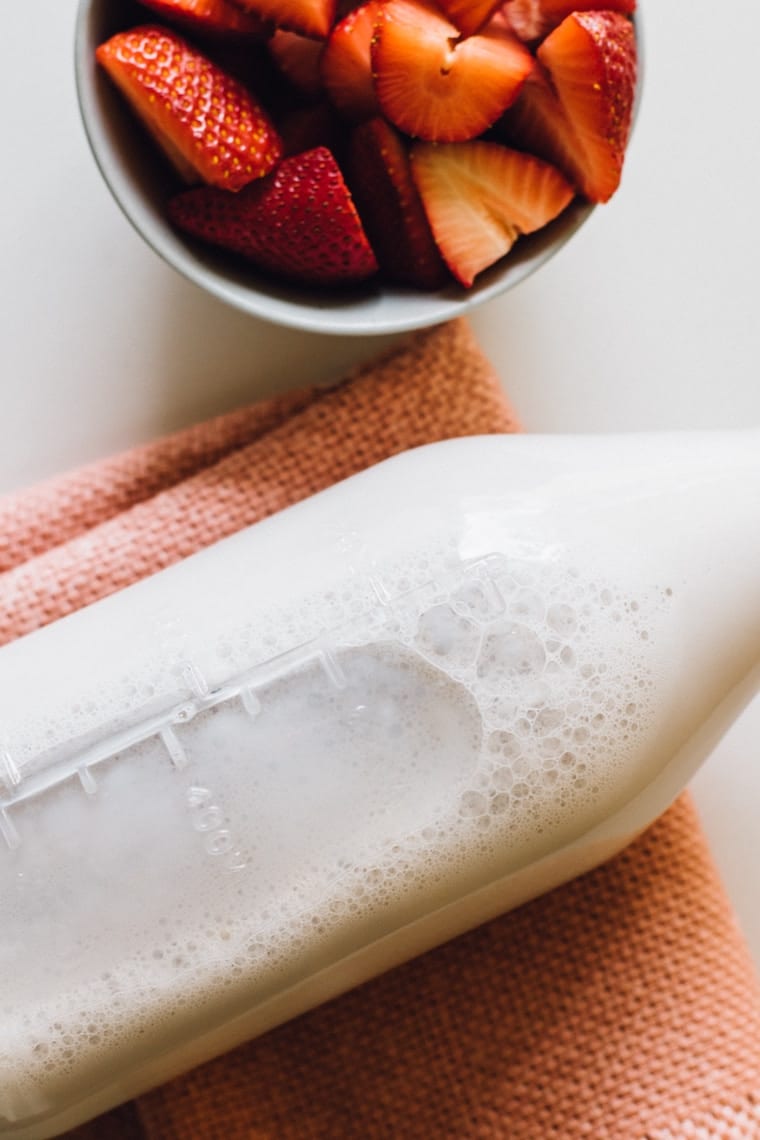 Milk in a bottle next to a bowl of strawberries. 