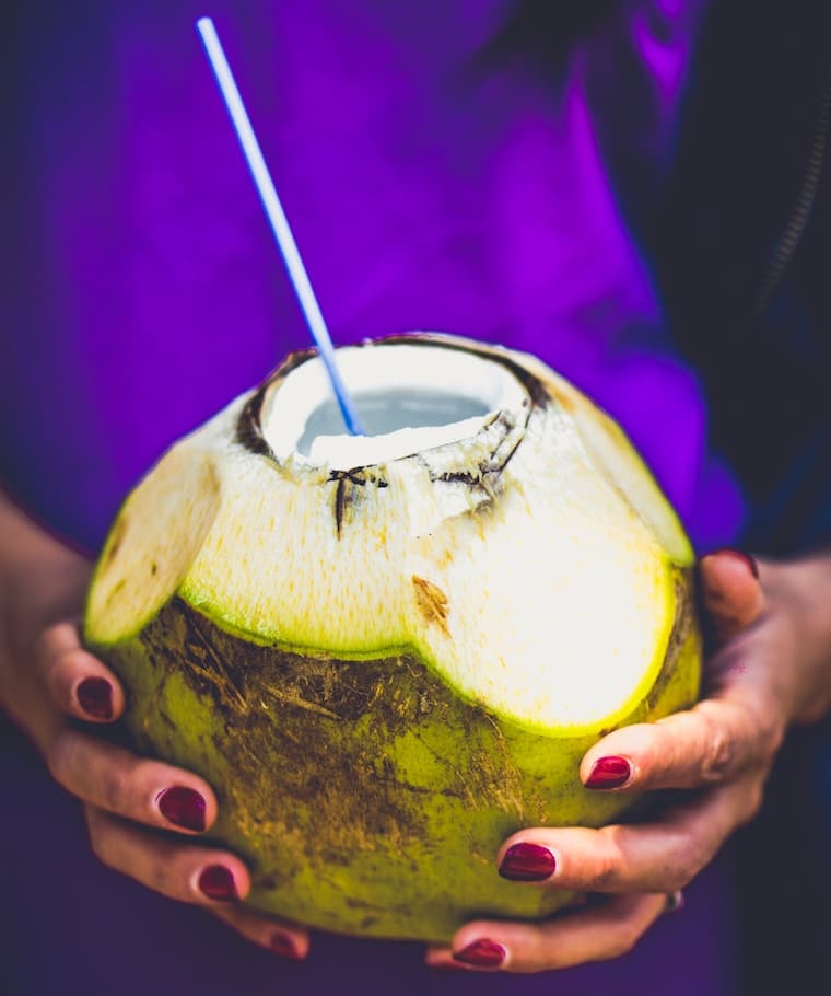 Women holding a coconut with a straw sticking out. 