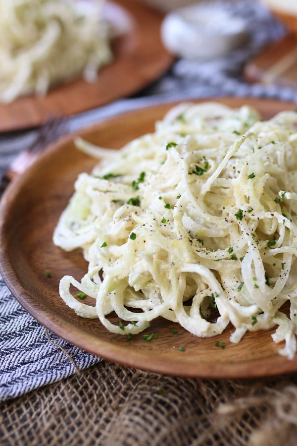 close up of vegan keto pasta alfredo on a wooden plate garnished with herbs 