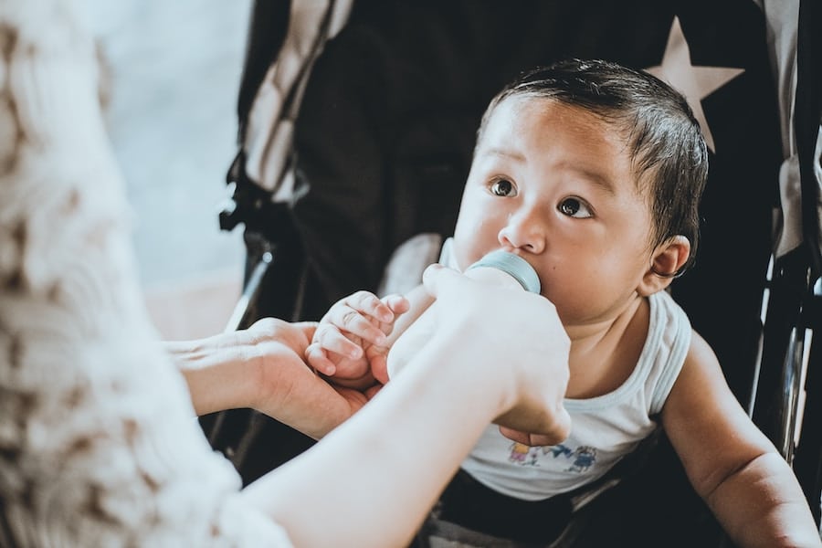 Baby in a stroller being fed a bottle.