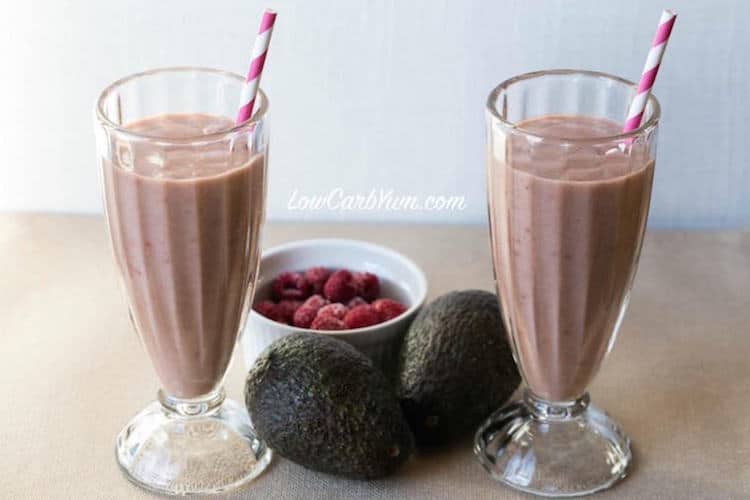 two tall clear glasses filled with keto raspberry avocado smoothie garnished with a pink and white straw 