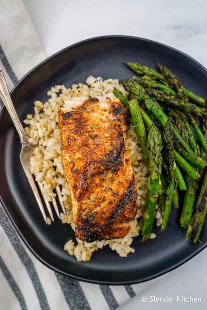 birds eye view of keto cajun salmon served with asparagus and cauliflower rice on a black plate