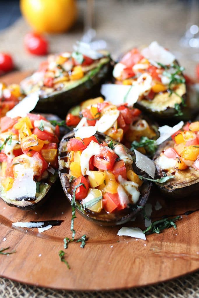 close up image of keto grilled avocado bruschetta on a wooden dish garnished with cheese and herbs