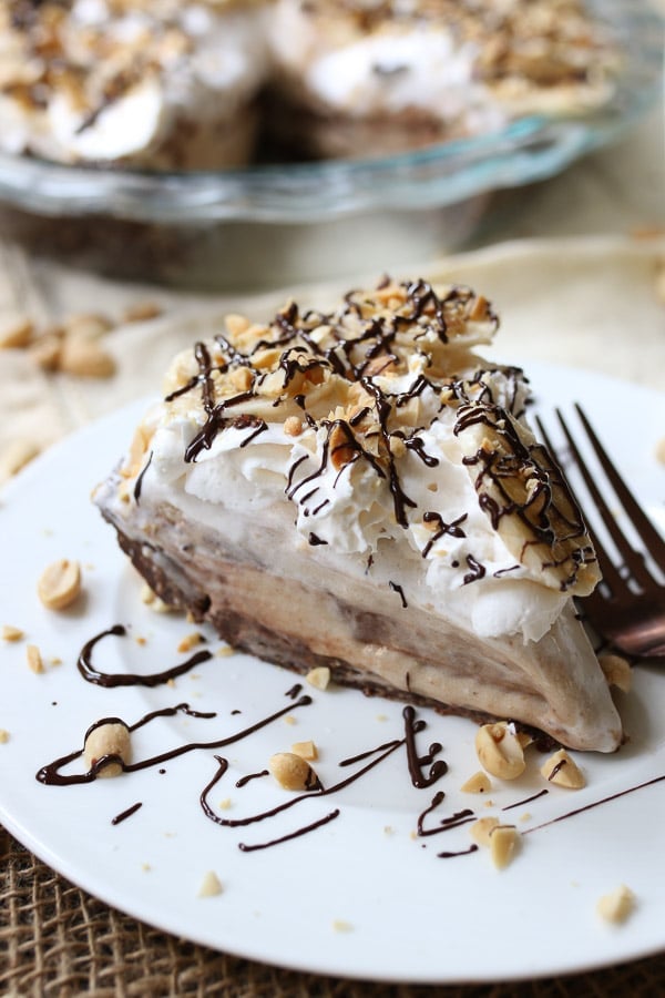 slice of no bake peanut butter and chocolate pie on a white plate topped with peanuts and chocolate