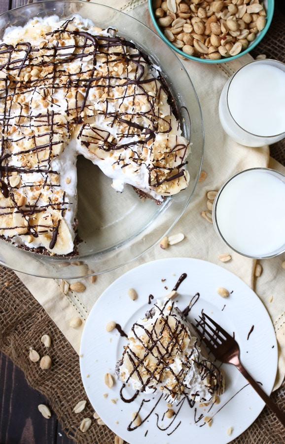 birds eye view of frozen peanut butter pie next to a slice of no bake pie on a white plate garnished with chocolate and peanuts