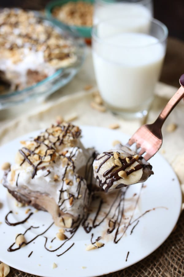 fork taking a bite out of no bake peanut butter pie garnished with chocolate drizzle on a white plate