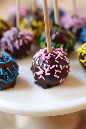Chocolate cake pop covered in pink sprinkles served on a white plate.