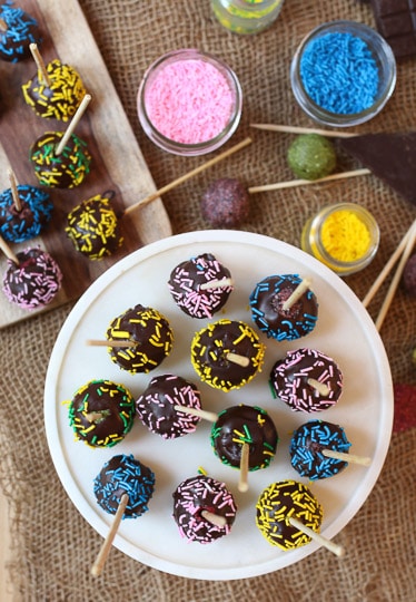 Chocolate cake pops covered in sprinkles served on a white plate.