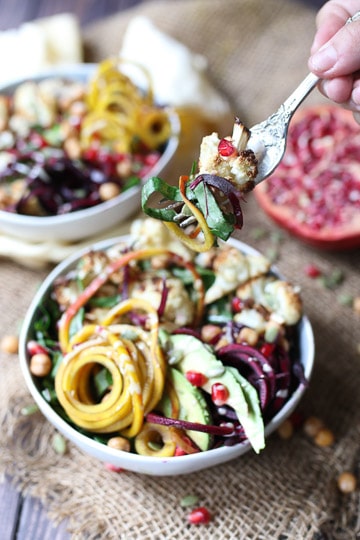 fork taking a bite out of vegan tahini power bowl in a white bowl topped with pomegranate seeds