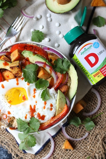 birds eye view of a buddha bowl garnished with cilantro and hot sauce next to a bottle of vitamin D supplements