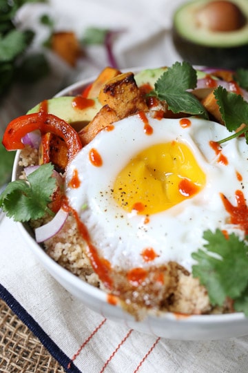 close up image of a sunny side up egg on a buddha bowl drizzled with hot sauce