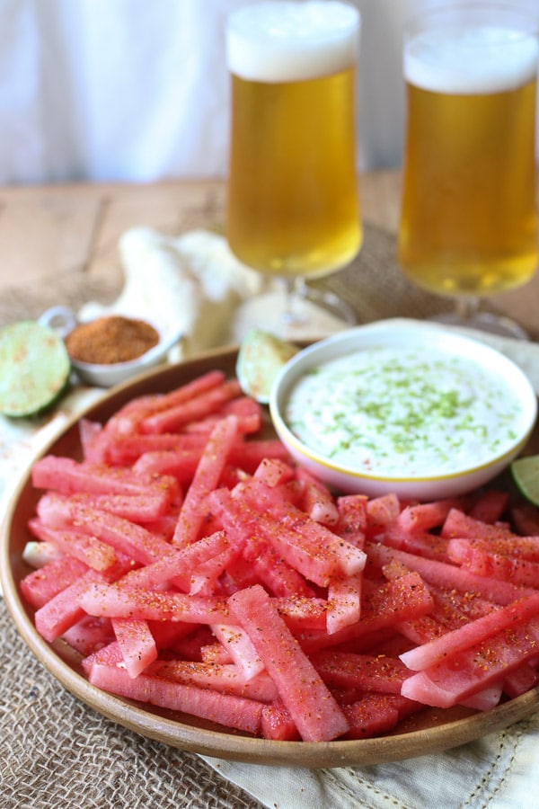 fruit sticks served on a wooden plate next to a dip.