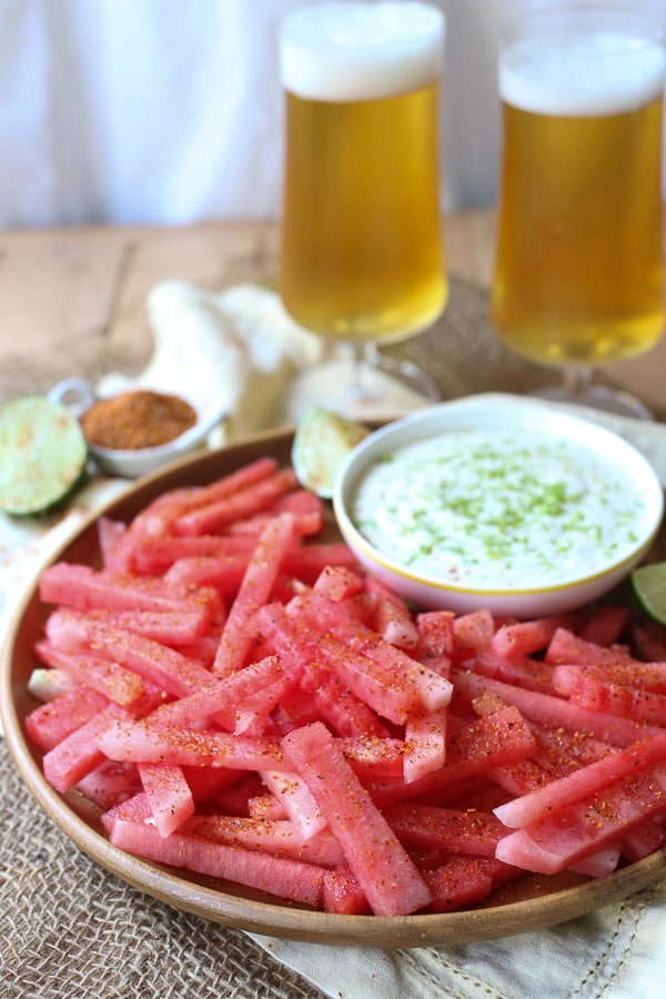 fruit sticks served on a wooden plate next to a dip. 