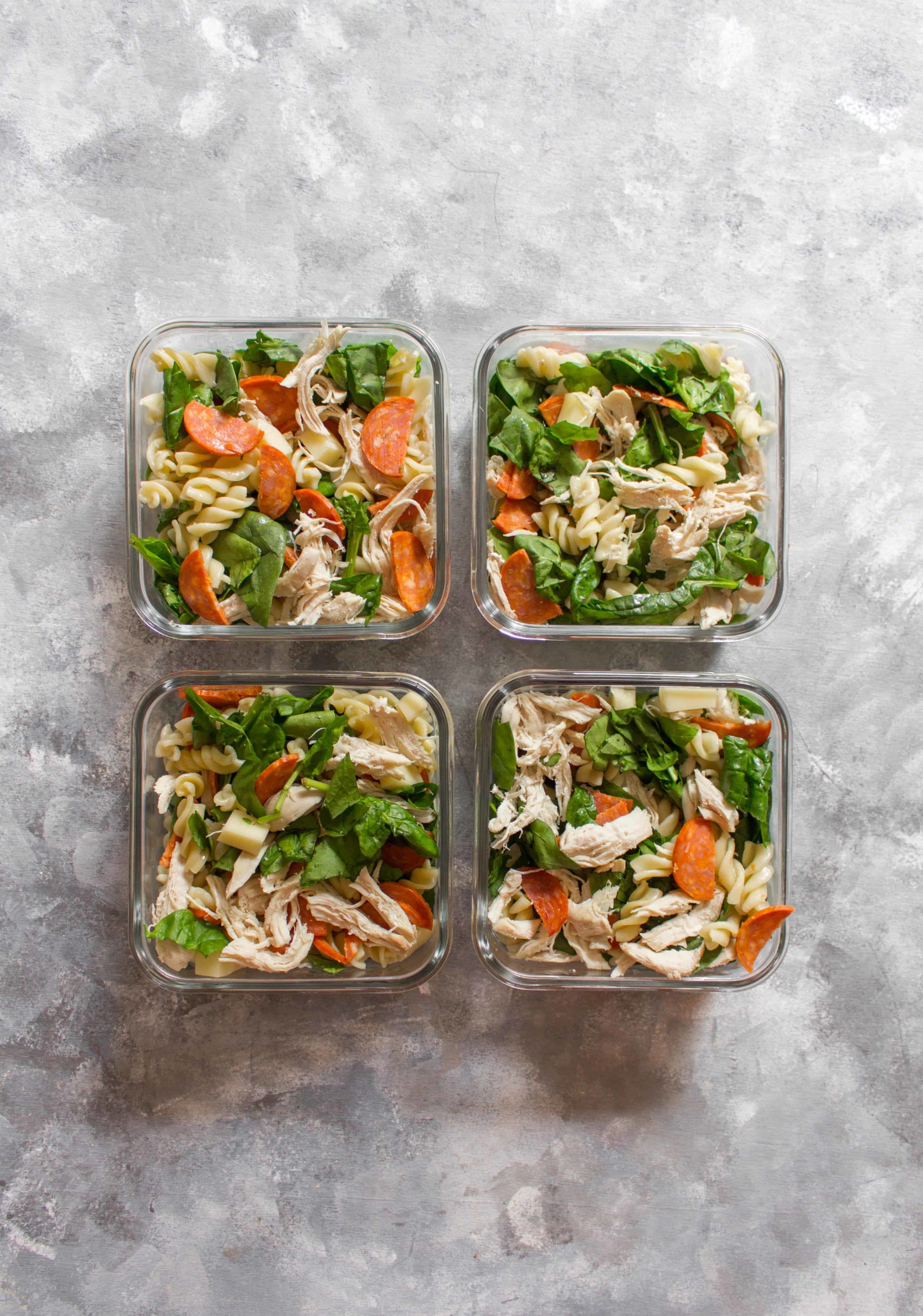 Pasta and veggies in four lunch boxes. 