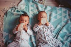 Two babies drinking from bottles while lying on a teal blanket.