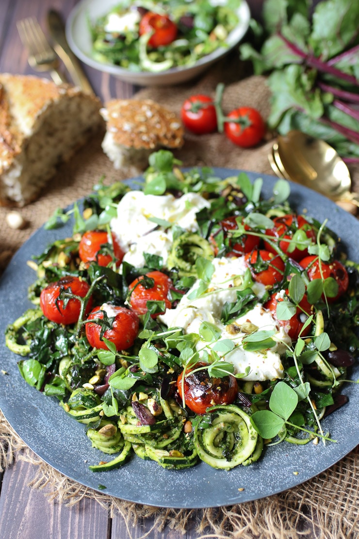 keto beet green pesto zoodles on a grey plate topped with tomatoes and cheese