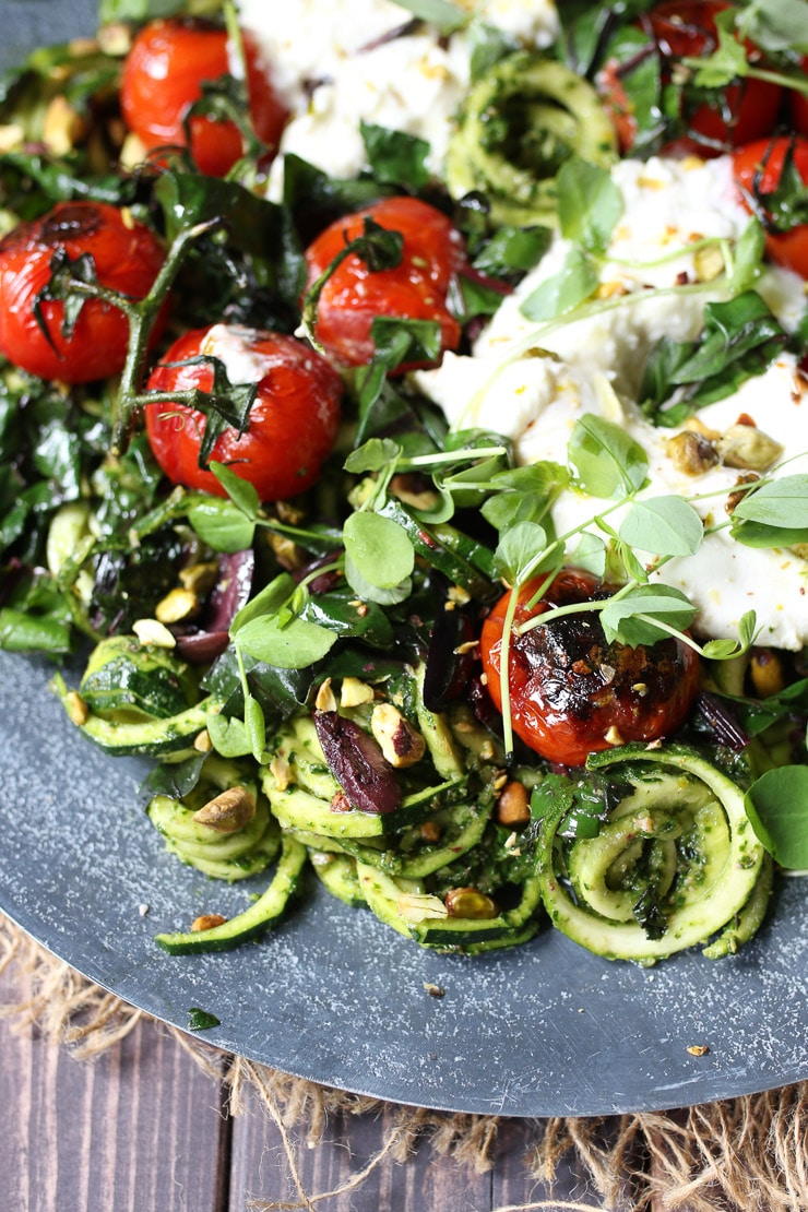 close up of keto pesto zoodles on a grey plate garnished with tomatoes and cheese