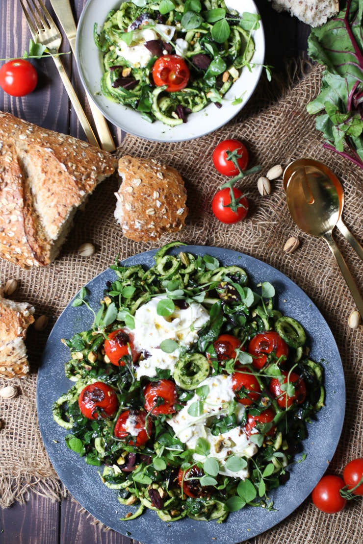 birds eye view of pesto zoodles topped with tomatoes and cheese on a grey plate next to a loaf of bread