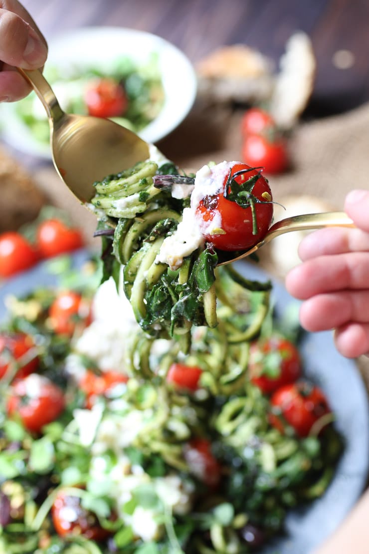 fork taking a bite out of keto beet green pesto zoodles garnished with tomatoes and cheese