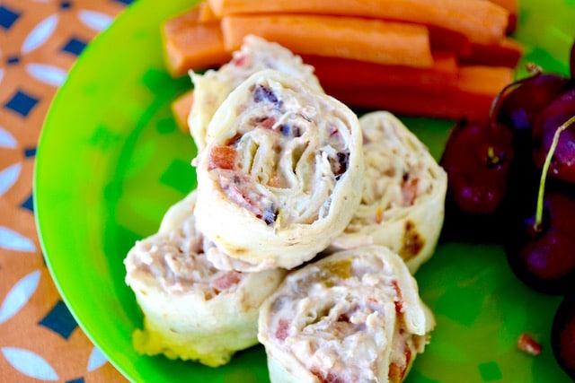 Pinwheel sandwiches on a green plate served with veggies. 