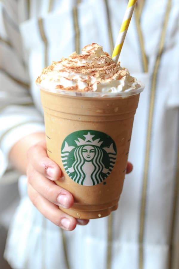 hand holding a starbucks cup with homemade pumpkin spice frappuccino topped with whipped cream and a straw 