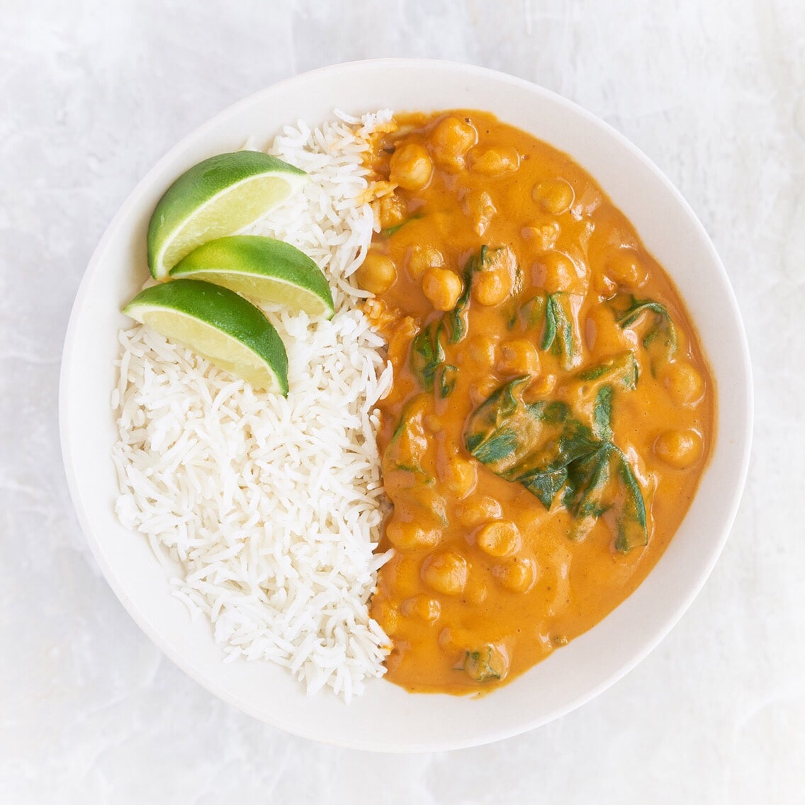 Bowl of white rice and curry with lime wedges. 