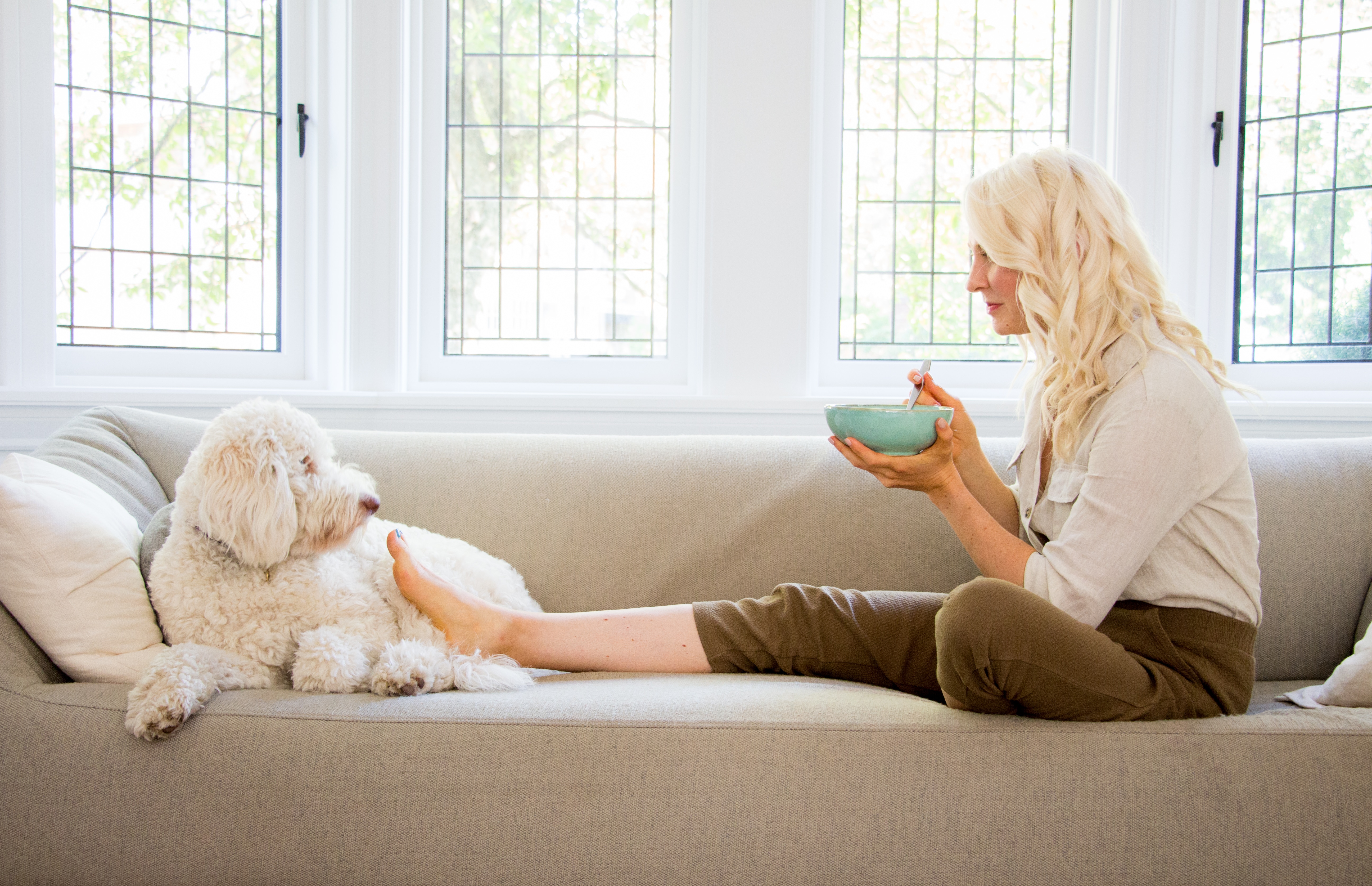 abbey holding a bowl sitting on the couch next to poppy