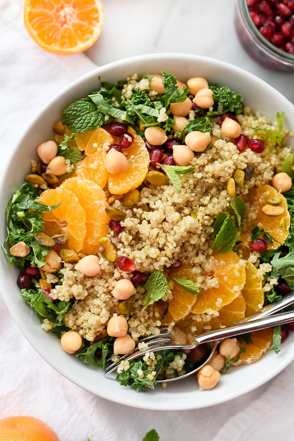 close up of gluten free quinoa and kale protein salad in a white bowl garnished with nuts and herbs