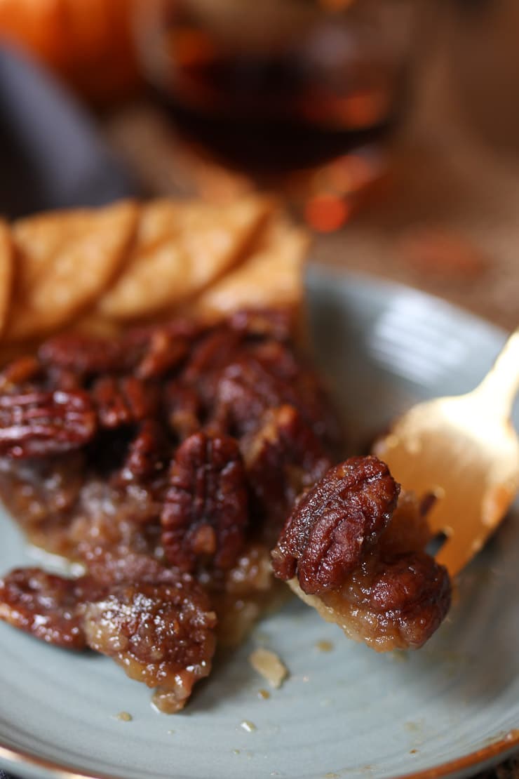 Close up of a fork taking a piece out of a pecan pie for thanksgiving on a grey plate.