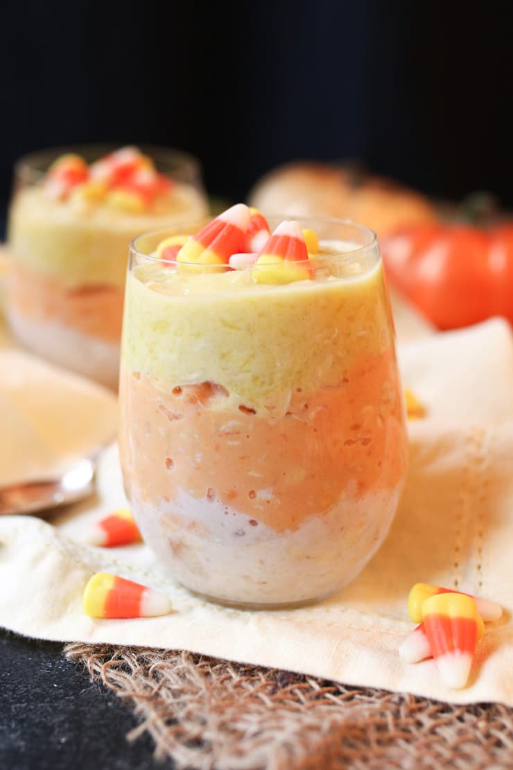 Glass jars filled with gluten free overnight oatmeal topped with candy corn on an orange cloth