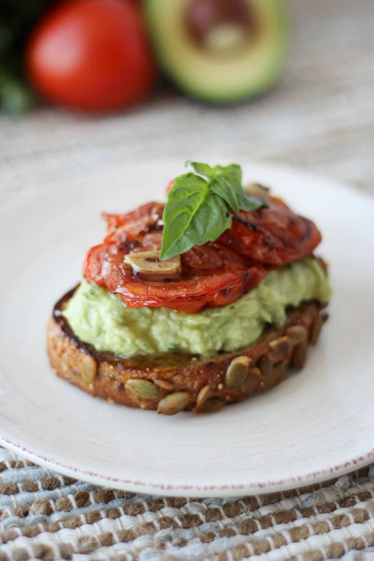 gluten free white bean avocado toast topped with roasted tomatoes and herbs on a white plate