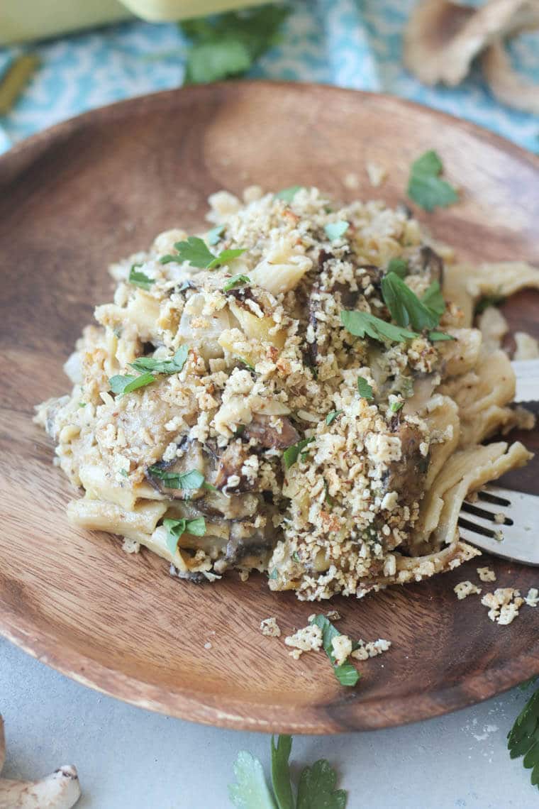 close up of gluten free mushroom pasta bake on a wooden plate topped with herbs 