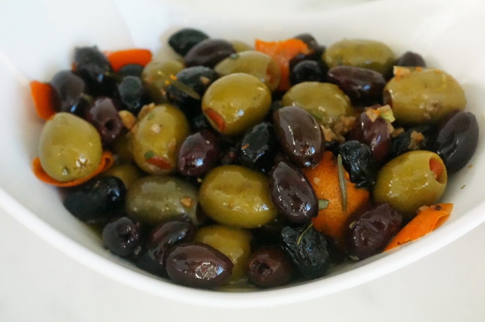 close up of gluten free blood orange and rosemary olives in a white dish