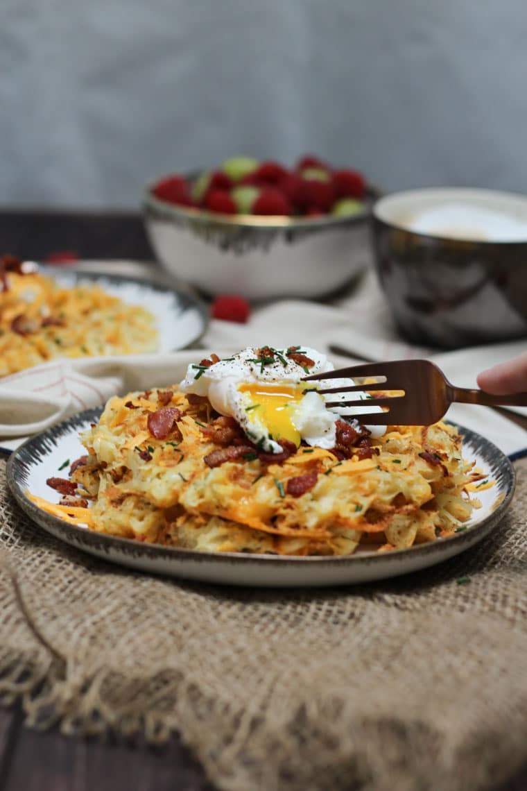 black and white plate containing gluten free potato waffles topped with a runny egg and bacon bits