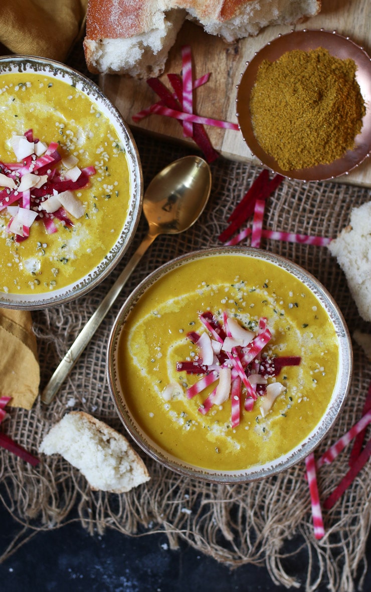 birds eye view of two grey and white bowls filled with vegan curry spiced beet and coconut soup garnished with beets, hemp hearts, and coconut