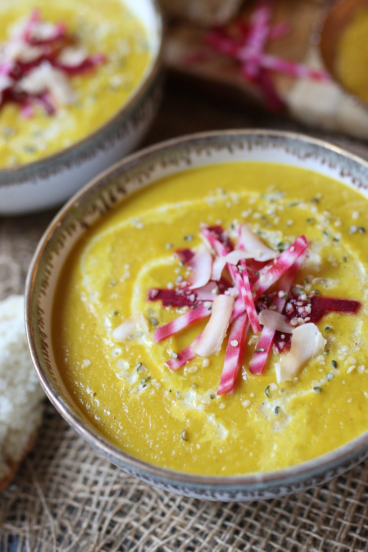 close up of curry flavoured vegan yellow beet and coconut soup garnished with beets, hemp hearts, and coconut