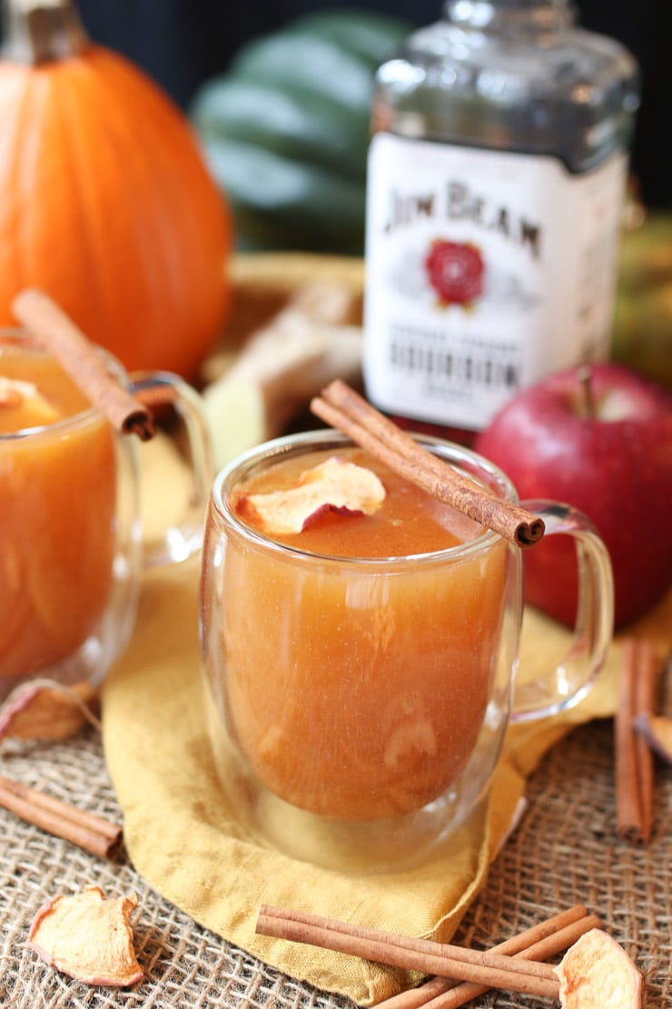 two clear mugs filled with healthy holiday cocktail garnished with an apple chip and cinnamon stick