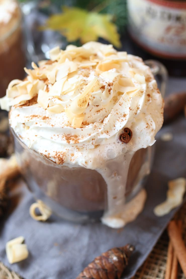 Warm vegan coconut rum cocktail in a clear mug garnished with whipped cream and cinnamon.