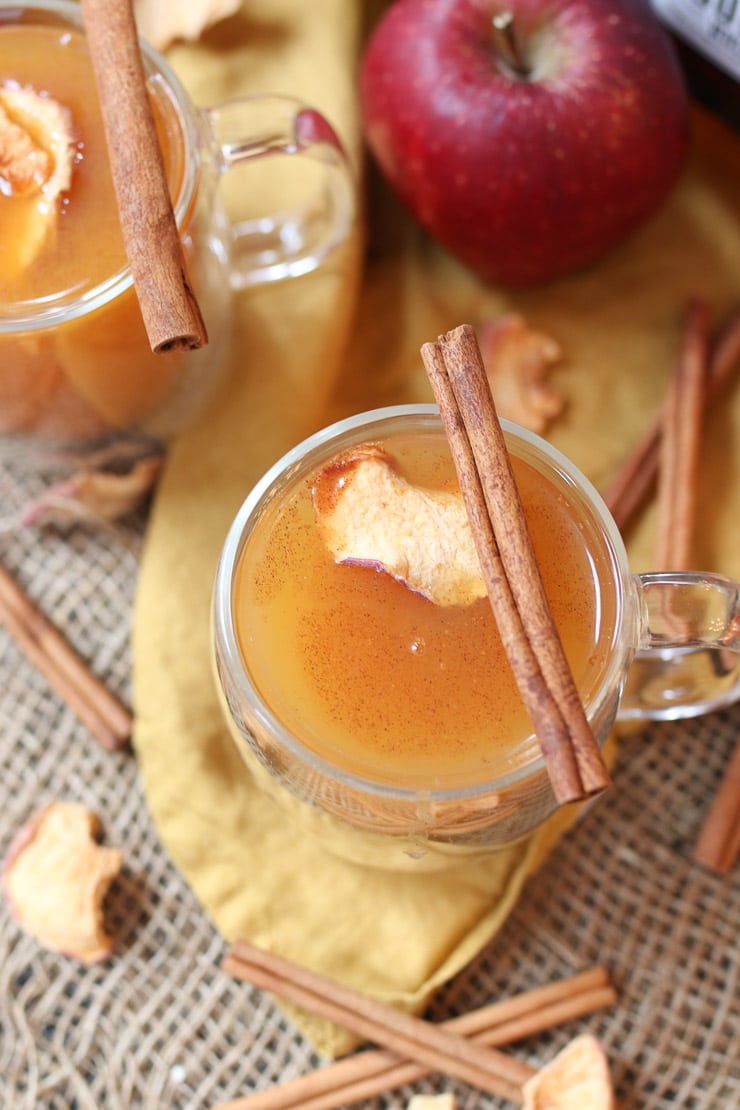 birds eye view of vegan pumpkin spice cider punch in a clear mug topped with an apple chip and cinnamon stick