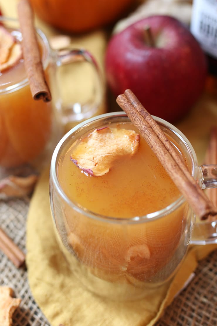 vegan pumpkin holiday cocktail in a clear mug with a cinnamon stick and apple chip