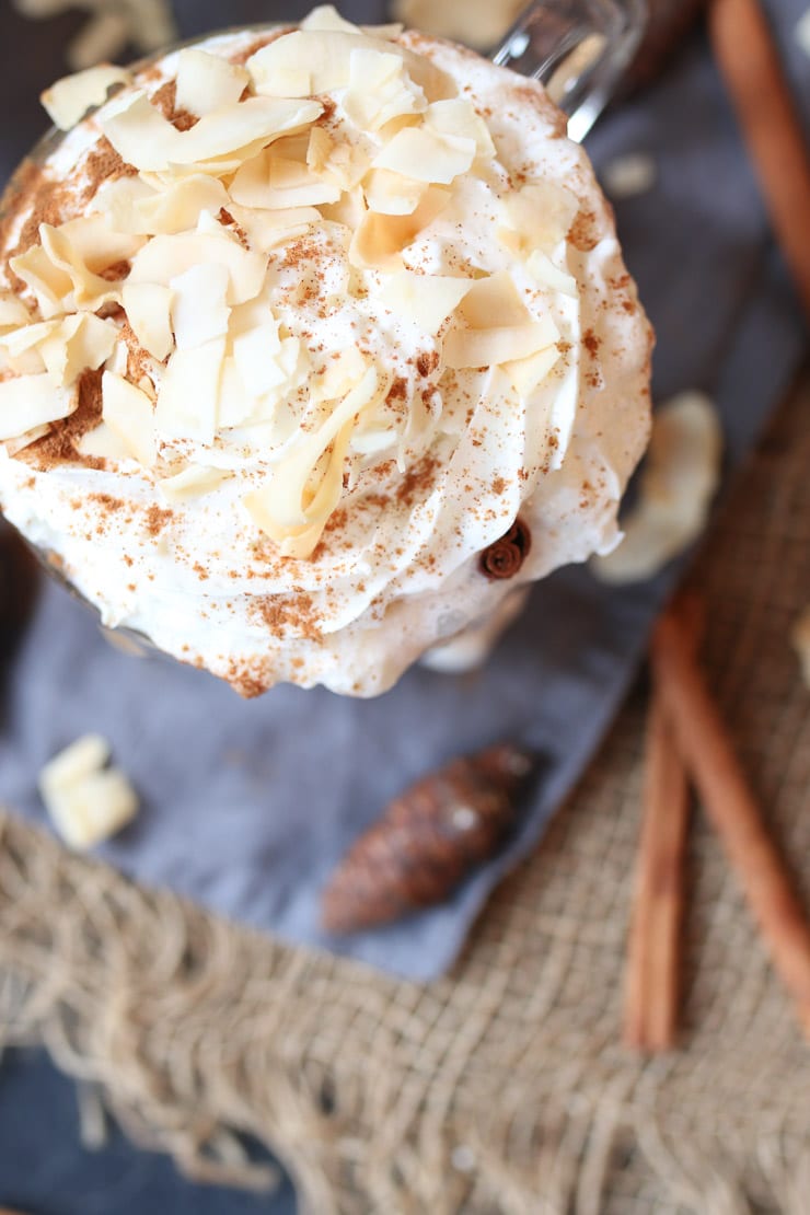 birds eye view of vegan coconut rum cocktail garnished with whipped cream next to a cinnamon stick