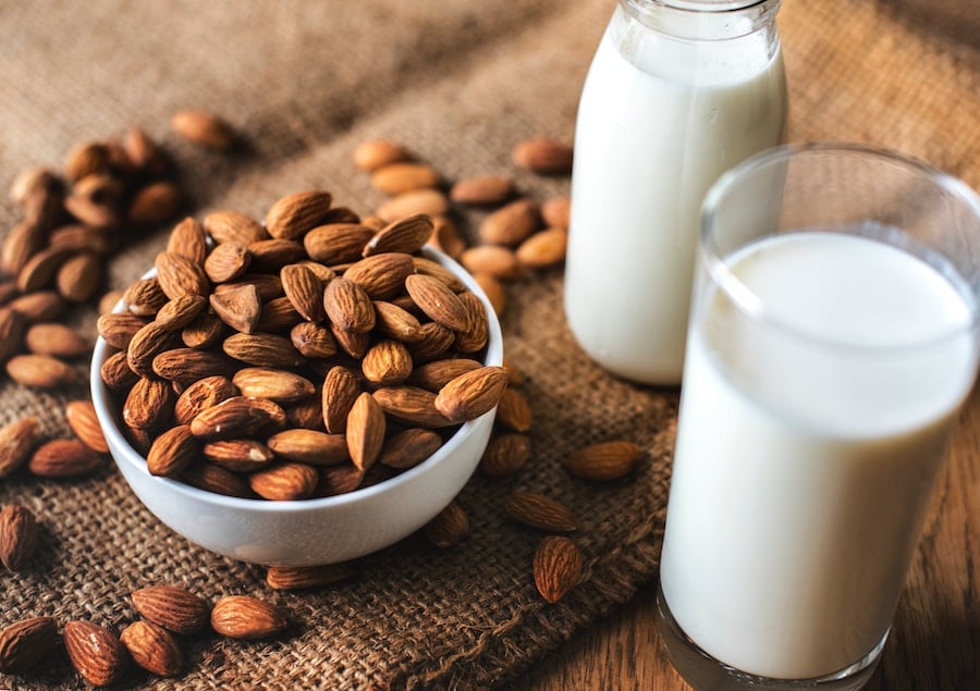 two jars filled with almond milk next to a bowl of almonds