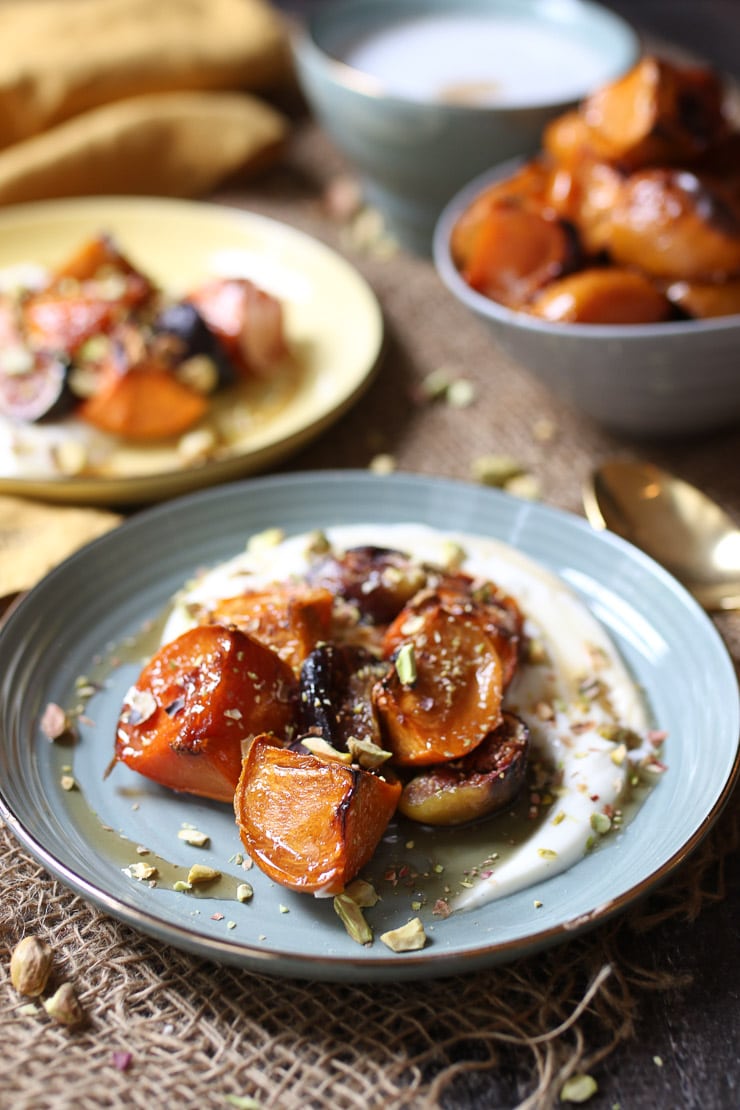 Roasted persimmons and figs on a teal plate with additional dessert in the background