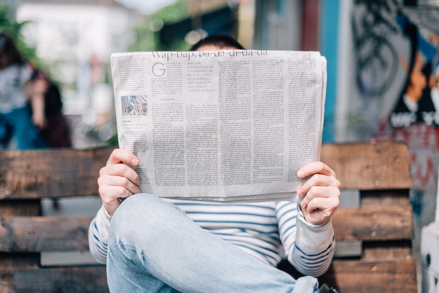 person reading a newspaper on a bench