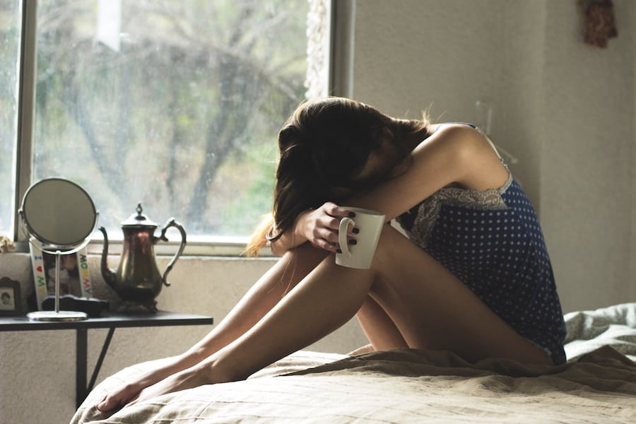 woman holding a mug looking sad on a bed