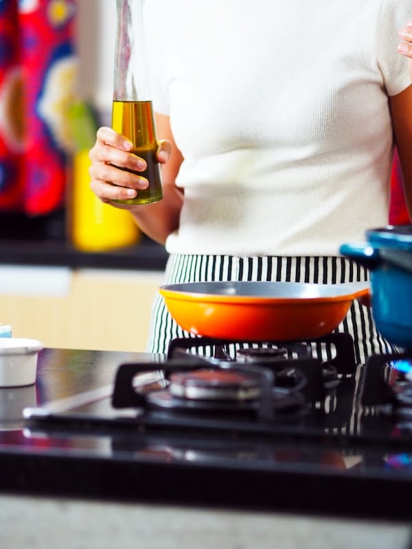 person standing above a stove with a red nonstick pan on it
