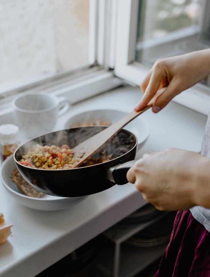 person serving a meal onto a plate from a nonstick pan